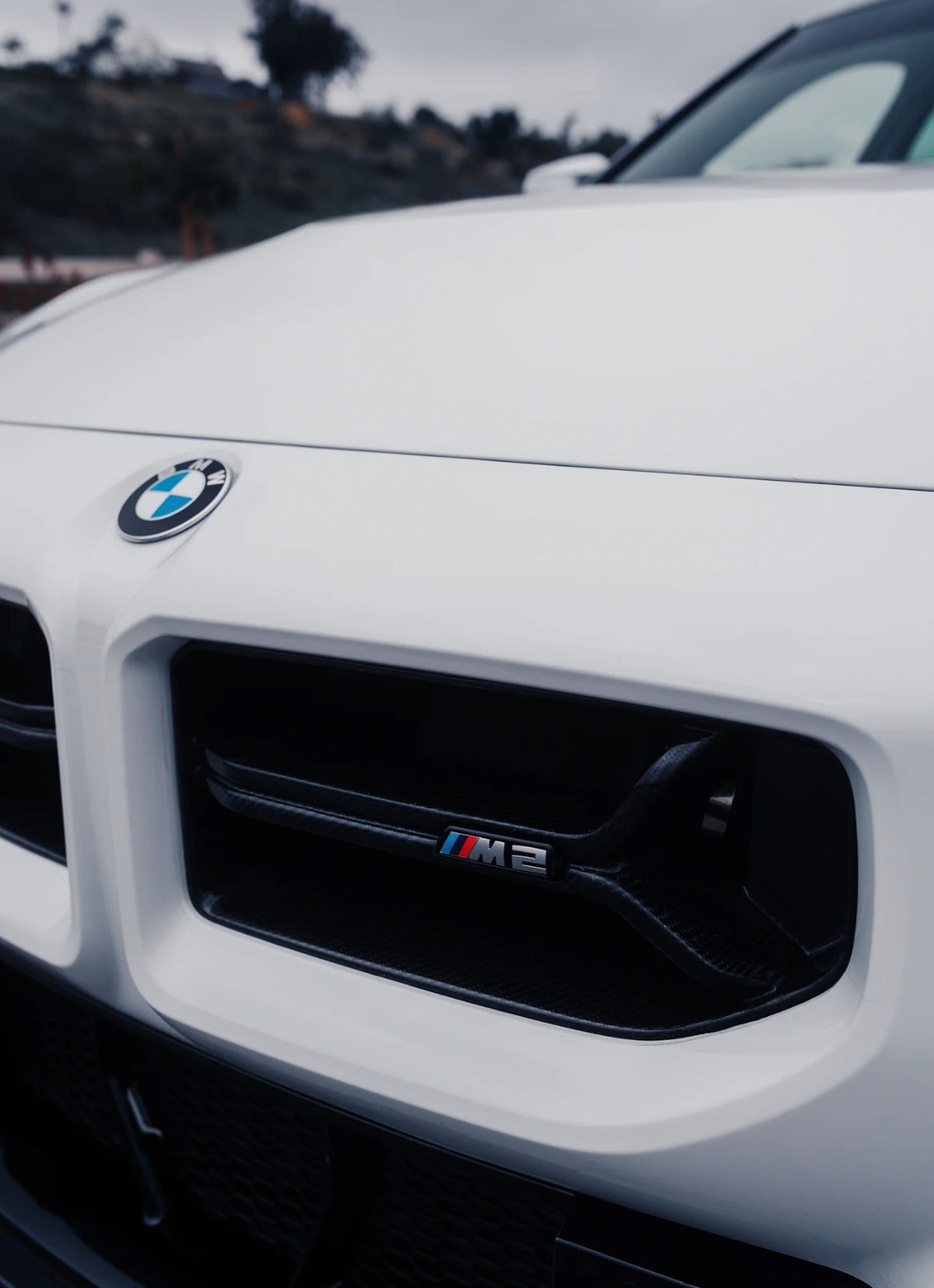 Weißer BMW M2 G87 mit V2 Carbon Frontgrill und markanter Performance-Optik.