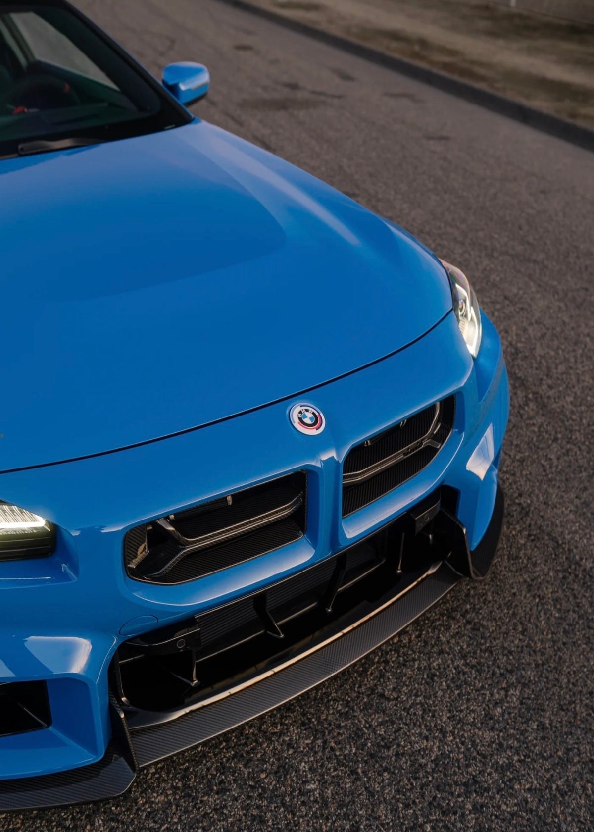 Blauer BMW M2 G87 mit CPG + V2 Carbon Frontgrill in sportlicher Frontansicht.

