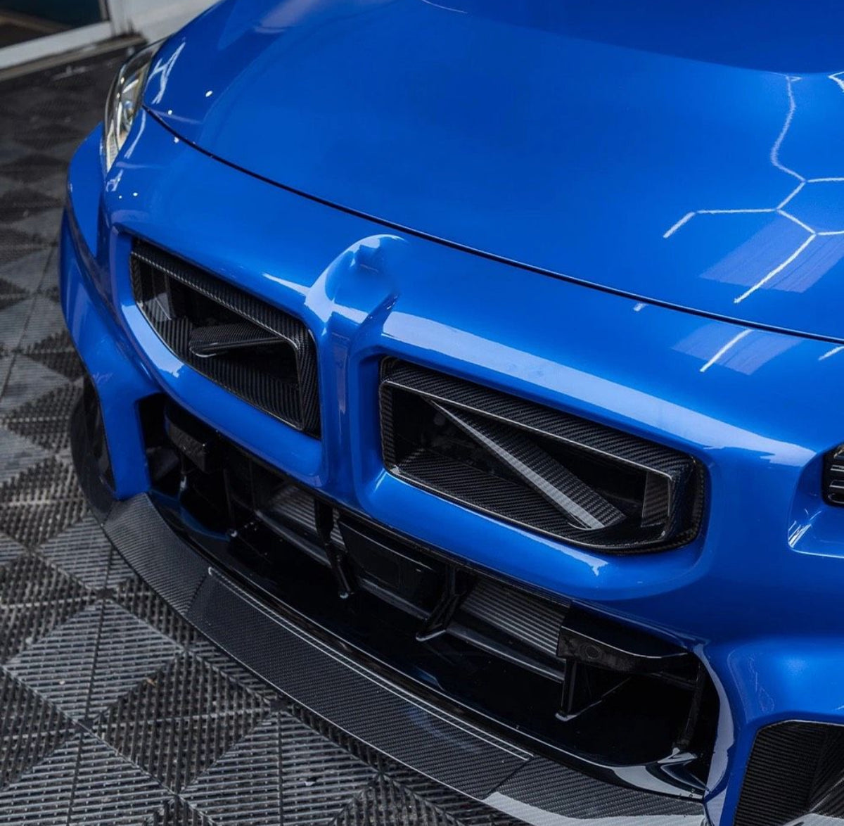 Blauer BMW M2 G87 mit montiertem CPG + V3 Carbon Frontgrill in sportlicher Frontansicht.