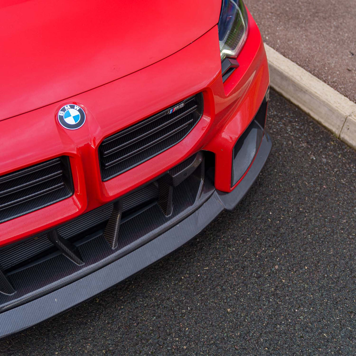 Detailaufnahme des CPG + V4 Dry-Carbon Frontgrills am roten BMW M2 G87 mit horizontalen Carbonlamellen und sportlicher Frontgestaltung.