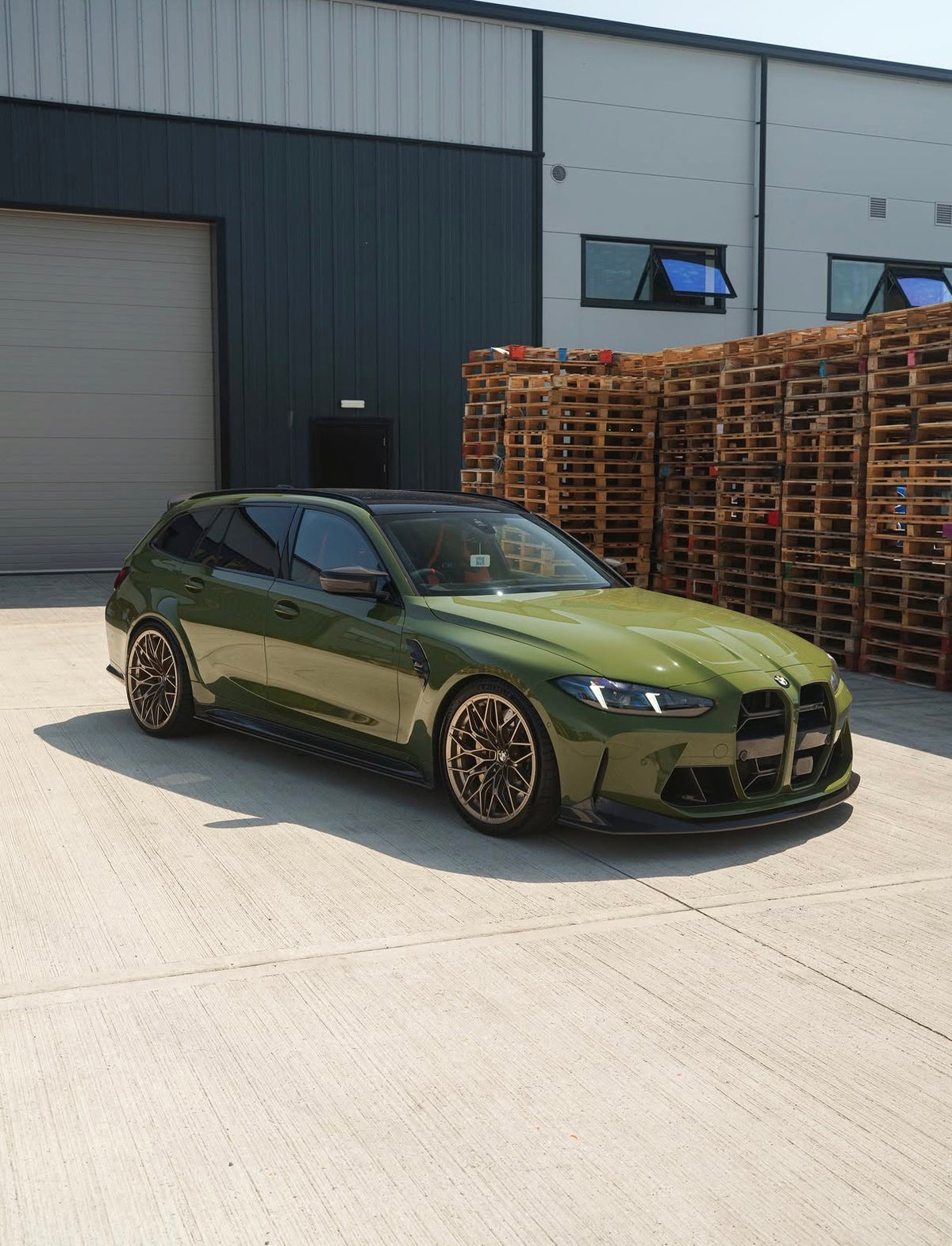 Grüner BMW M3 G80 mit CPG+ V6 Carbon Seitenschwellern und Seitenschwelleransätzen vor einer Halle