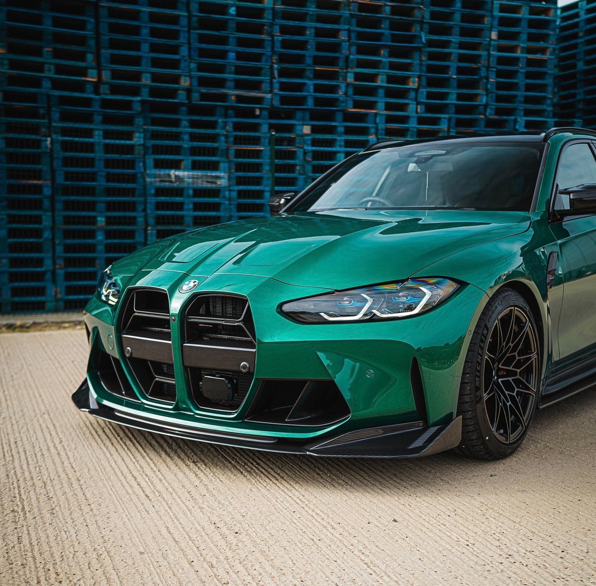Grüner BMW M3 G80 mit CPG+ V9 Carbon Frontlippe vor einer modernen Gebäudefassade