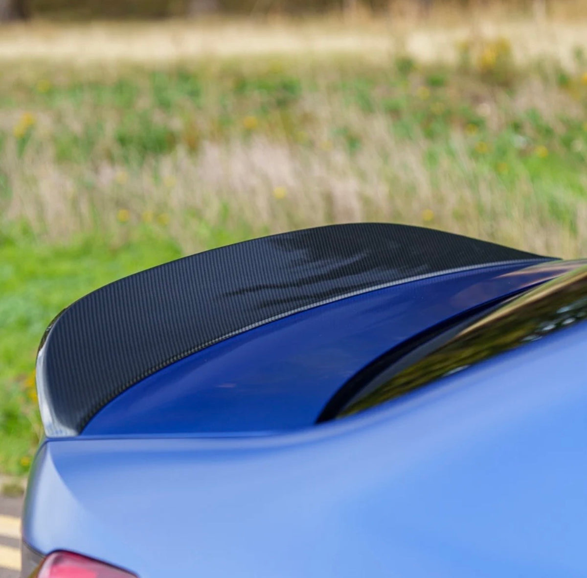 Detailaufnahme des V8 Heckspoilers auf der Kofferraumklappe eines blauen BMW M3 G80